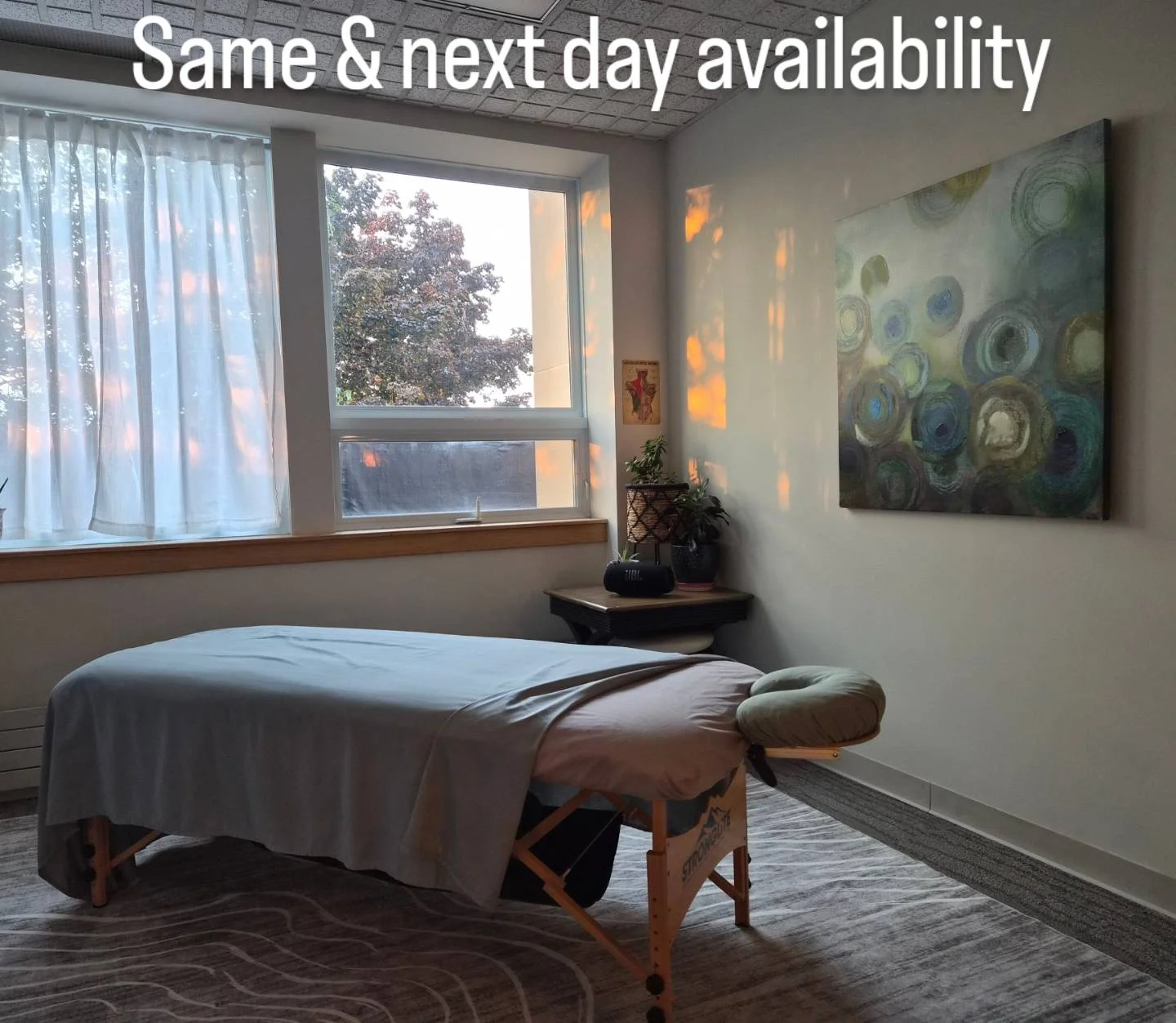 Same and next day availability. Treatment room with a massage table beside windows and abstract wall art.