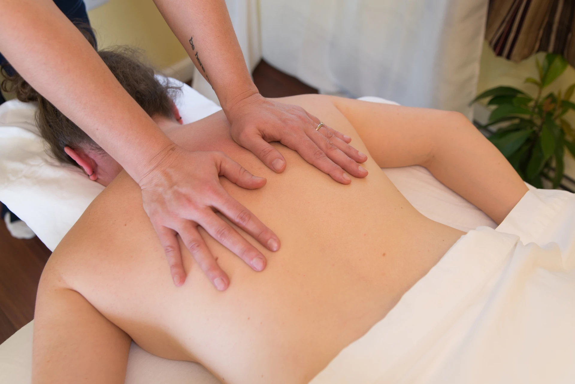 A massage therapist applies steady hands-on pressure across a patient's back during a medical massage session