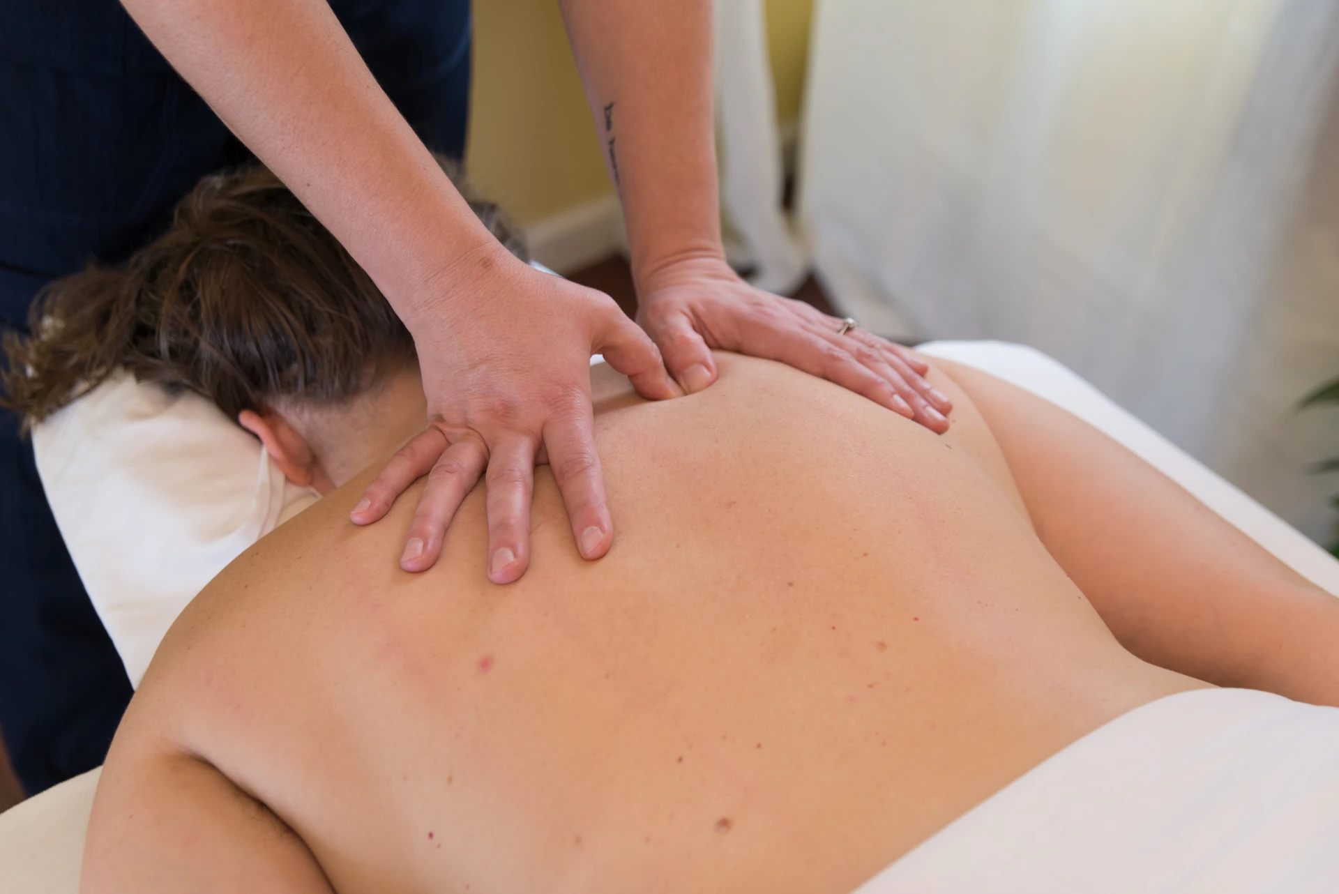 A massage therapist applies broad, hands-on pressure across a patient's upper back during a medical massage session
