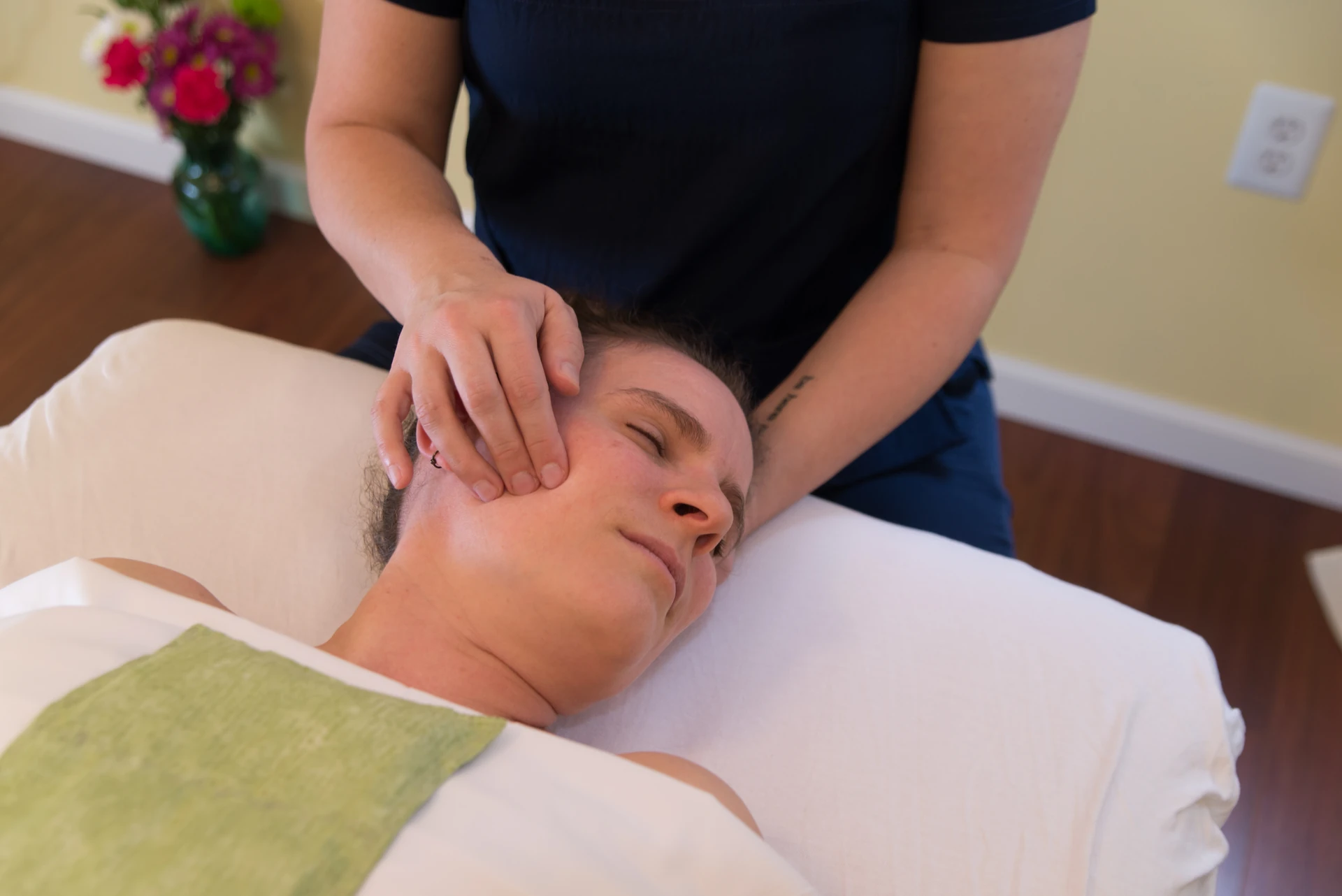 A massage therapist works gently along a patient's jaw and cheek during a focused TMD massage session.