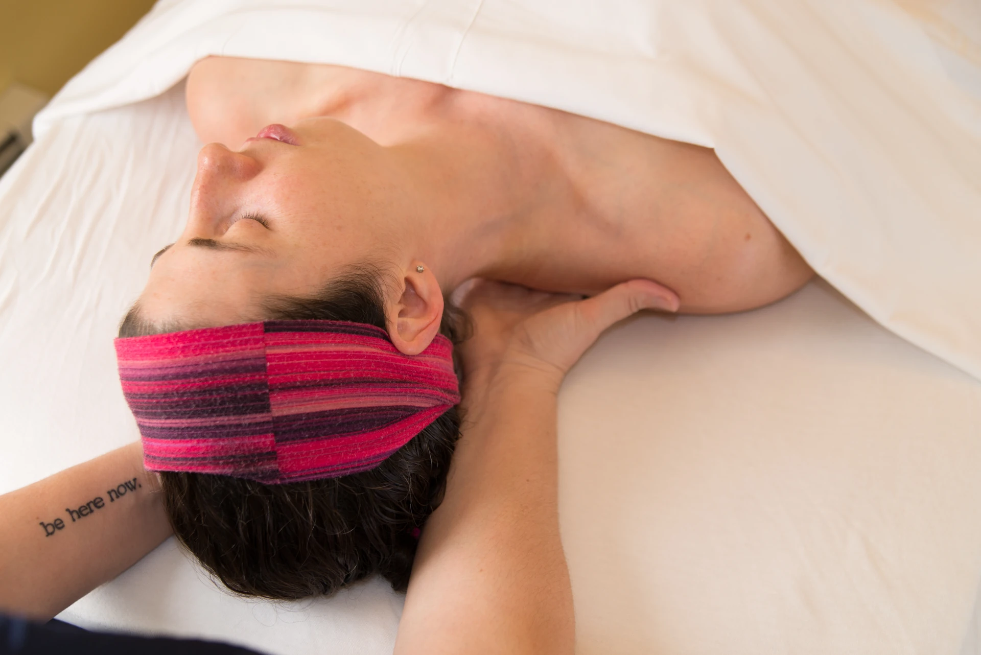 Close view of a massage therapist cradling and releasing tension at the base of a patient's neck during a calm medical massage session.