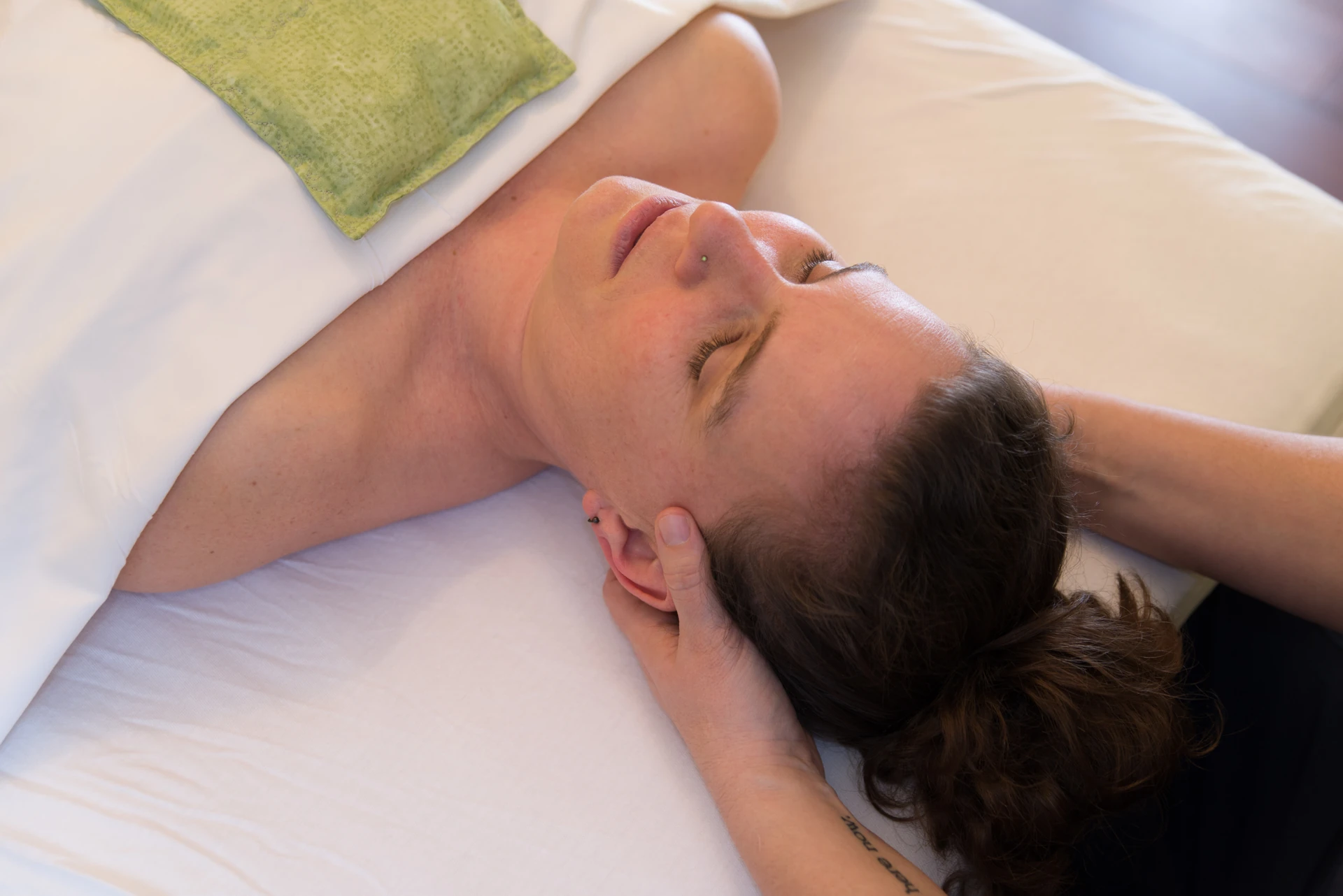 A massage therapist gently cradles and supports a patient's head and neck during a calm, unhurried medical massage session.