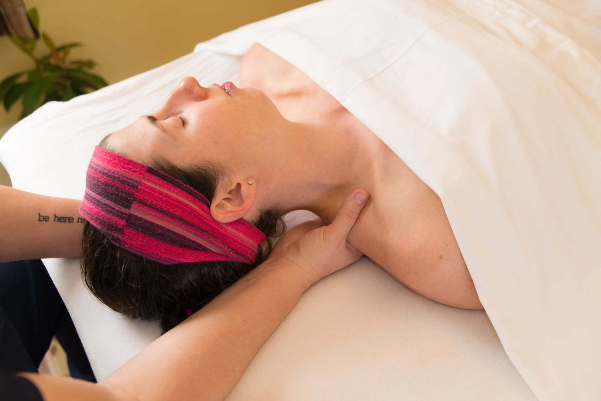 A massage therapist supports and works along a patient's neck and shoulder during a hands-on neck pain massage session.