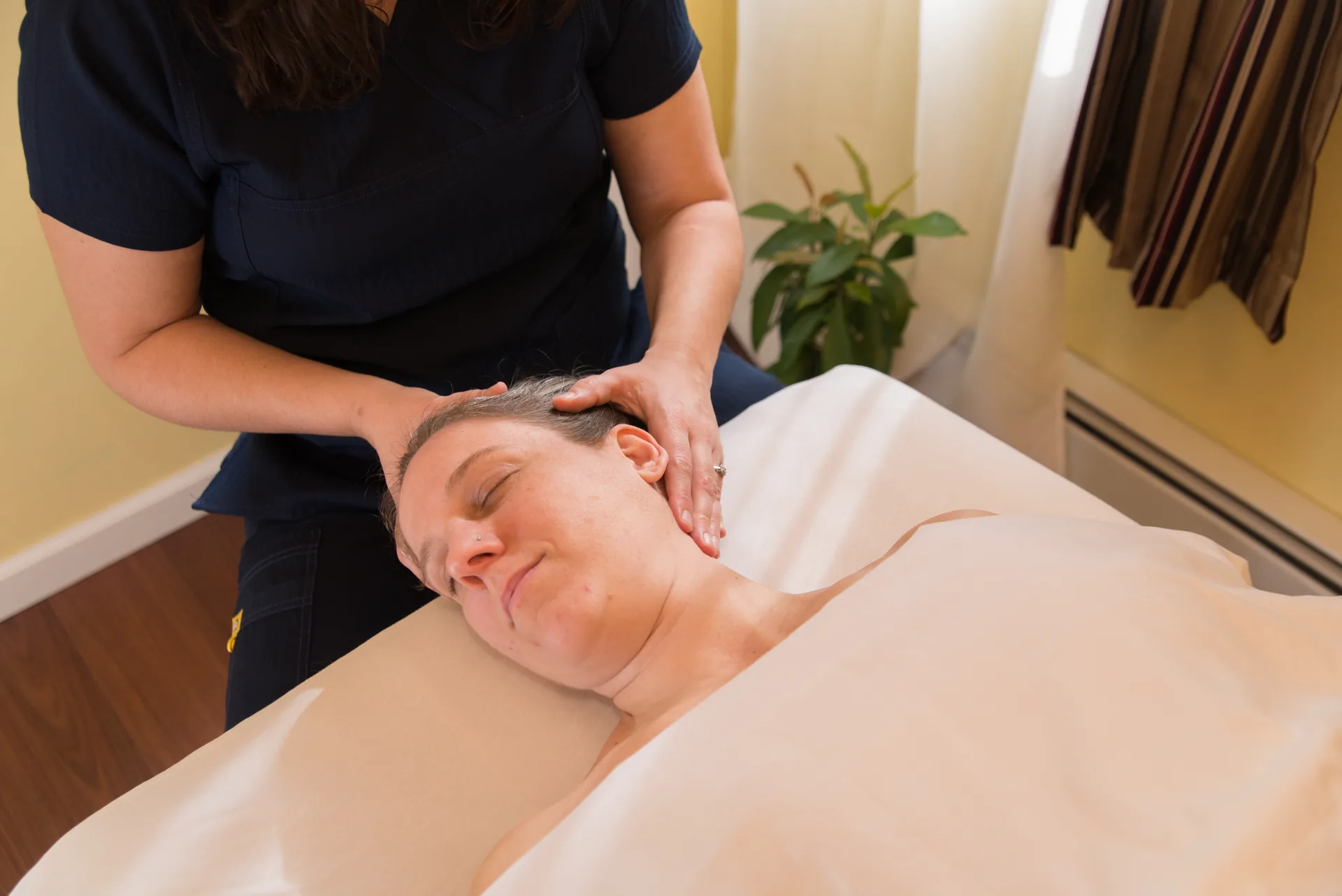 A massage therapist cradles the head and neck of a smiling patient in the treatment room during a calm medical massage session.