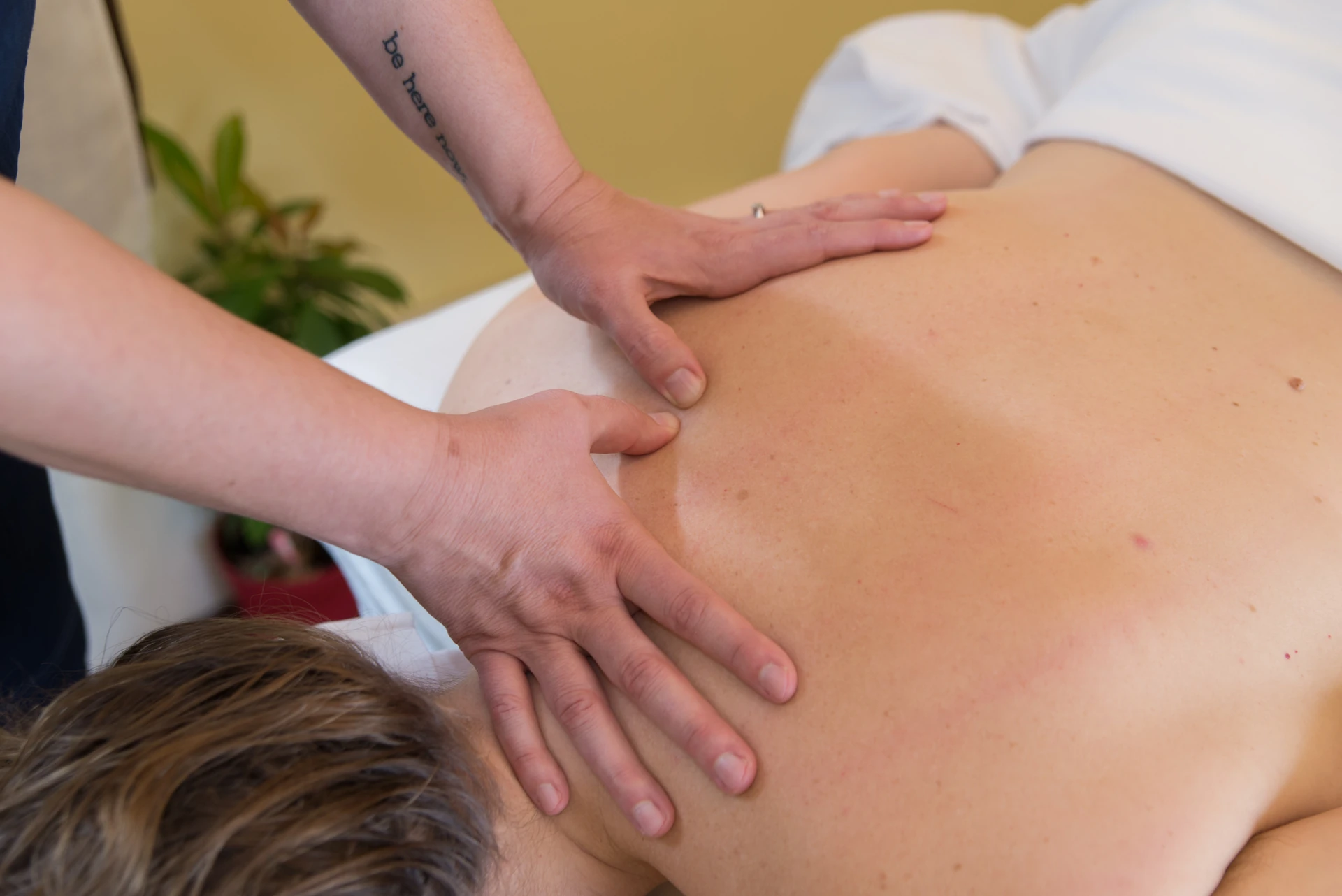 A massage therapist applies focused pressure across a patient's upper back and shoulder during a hands-on medical massage session.